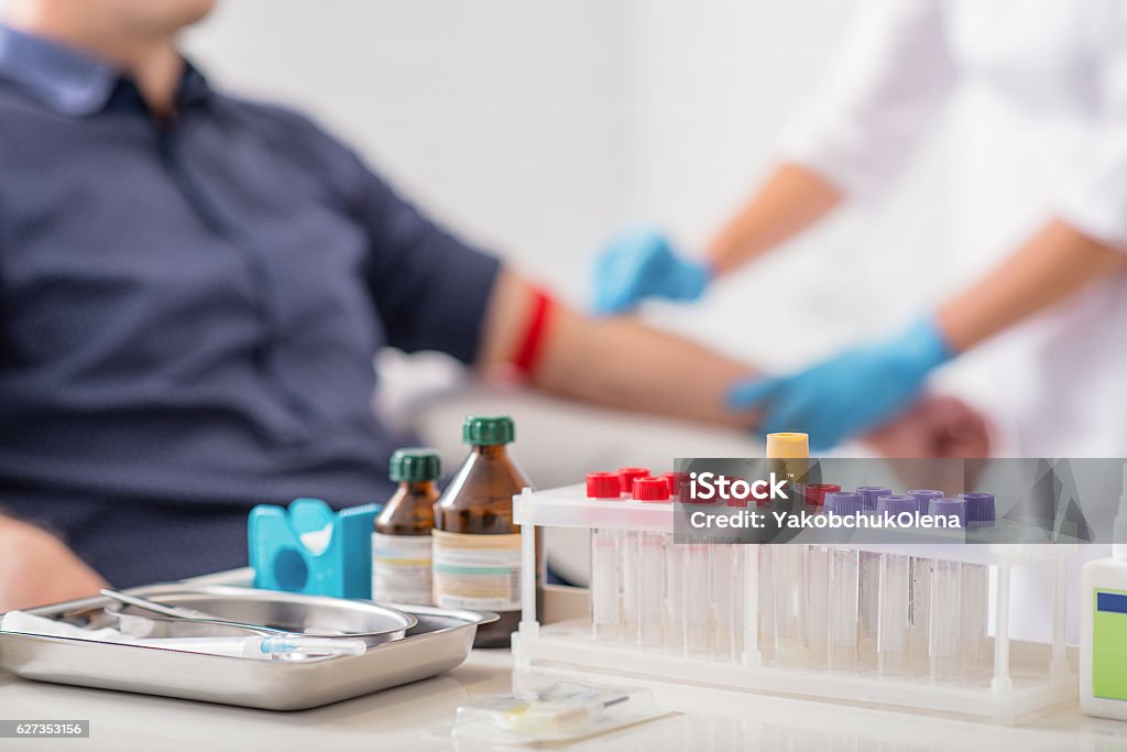 Man getting blood test preparation in clinic Doctor preparing patient for blood sampling. Focus on blood test tools on table Scientific Experiment Stock Photo