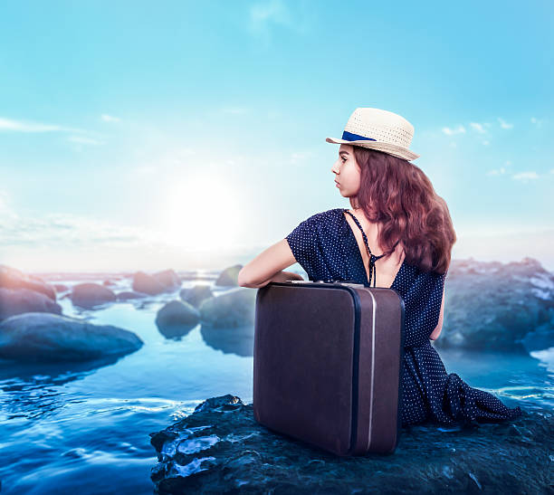 istock Young girl with suitcase sits on a stone. 627353502