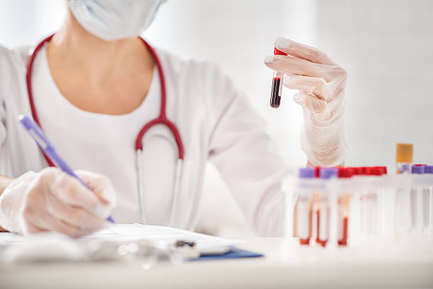 Skillful female scientist making experiment Close up of doctor arms holding blood test tube and making notes. Woman is sitting at table in lab bloody money stock pictures, royalty-free photos & images