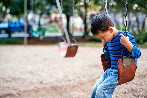 Young boy sitting on swings alone looking sad Young boy sitting on swings alone looking sad child abuse stock pictures, royalty-free photos & images