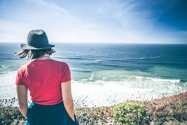 jeune femme regardant au-dessus de l’océan. - hiking young women outdoors t shirt photos et images de collection