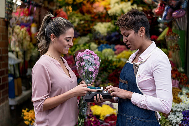 femme effectuant un paiement sans contact chez le fleuriste - florist telephone flower business photos et images de collection