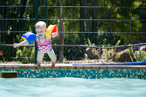 Jubilant baby girl with water wings jumps into the swimming pool