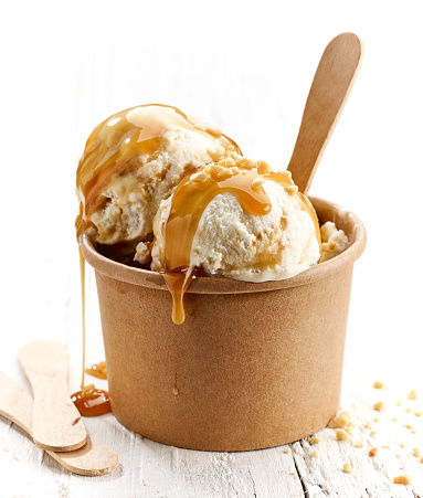 ice cream with caramel sauce and ground nuts on white wooden table