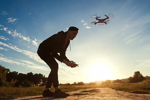 Piloting drone in field, sunset flare, free space. Young man running quadrocopter outdoor on blue sky background. Leisure, entertainment, modern technologies concept