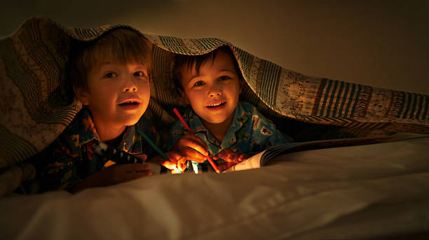 Just five more minutes! Two young brothers coloring in pictures while underneath their blanket after their bedtime slumber party stock pictures, royalty-free photos & images