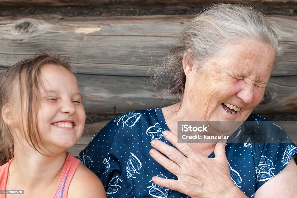 elderly woman with the grand daughter The elderly woman with the grand daughter against the wooden house Grandparent Stock Photo