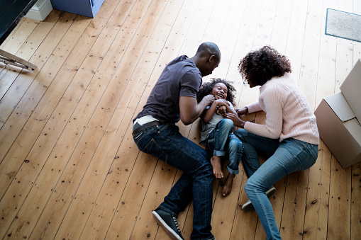 A photo of cheerful parents playing with son at new home. High angle view of family lying on hardwood floor. All are in casuals.