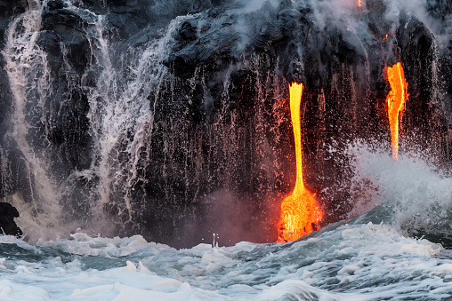 Molten lava flowing into the Pacific Ocean on Big Island as waves and water wash off the cliff along with lava
