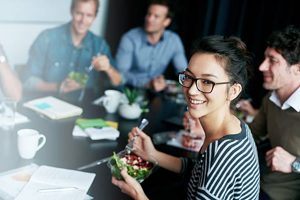 Enjoying a team lunch! Portrait of a young office worker eating lunch with coworkers at a boardroom table group of people wearing eyeglasses stock pictures, royalty-free photos & images