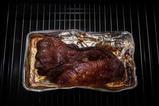 Crispy fried duck breast in an aluminum pan on the rack in the kitchen oven, dark background with copy space, selected focus, narrow depth of field