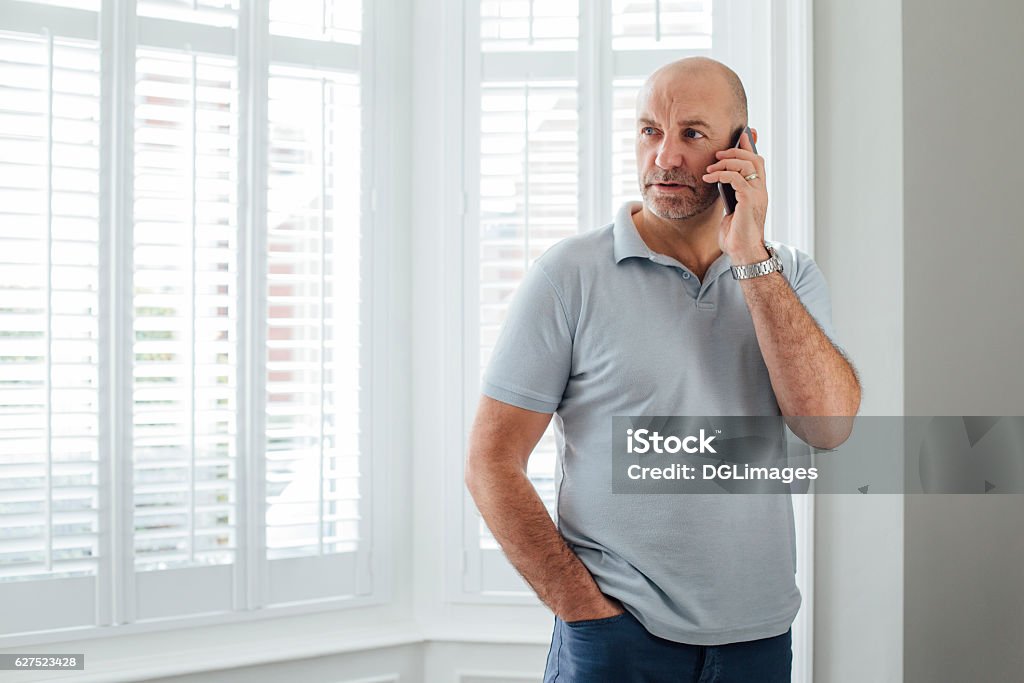 Talking on the Phone Man talking on the phone. He is standing by the window in his home with a serious expression. Using Phone Stock Photo