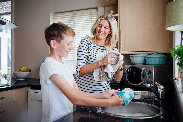 Mother and Son Doing the Dishes Mother and son doing the dishes together. They are talking and laughing as the boy washes and the mother dries dishes. pre adolescent child stock pictures, royalty-free photos & images