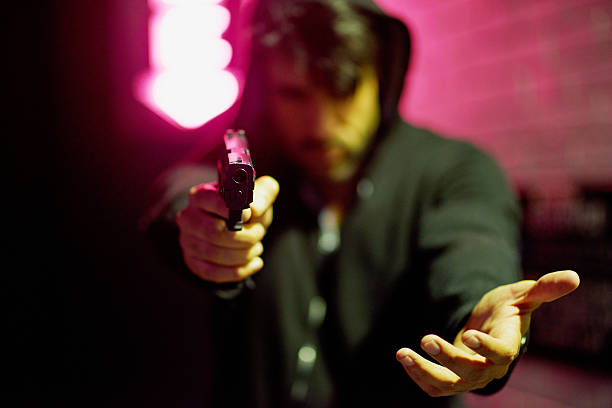 Crime is rife in all big cities Portrait of a gun-wielding thief aiming his weapon man holding gun at night in the city stock pictures, royalty-free photos & images