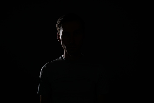 Young caucasian man in t-shirt on dark background.