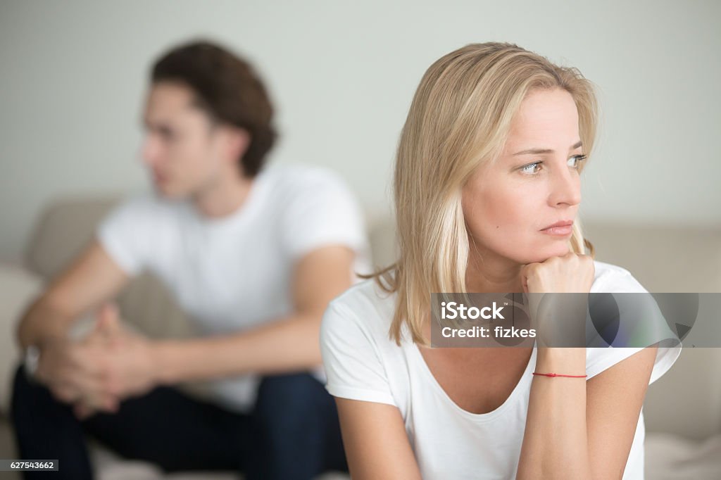Sad woman thinking over a problem, man sitting aside Serious sad woman thinking over a problem, man aside, meeting therapist, poor chance of getting pregnant after 40, unmet expectations, unable to handle family finances, interested in different things Couple - Relationship Stock Photo