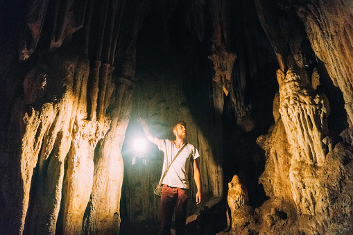 Young Caucasian man standing in the cave with lantern, Thailand 