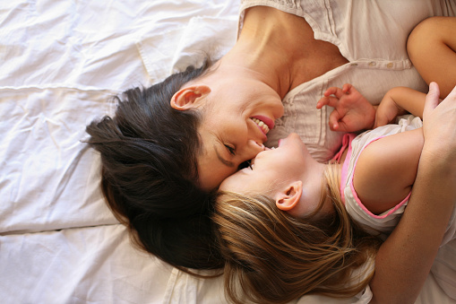 Young  mother and daughter laying in bed together at home.