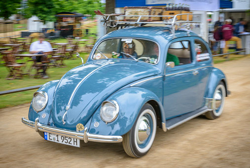 Jüchen, Germany - August 5, 2016: Volkswagen Beetle or VW Bug with a roof rack and ski's suitcases driving by at high speed on a country road. The car is on display during the 2016 Classic Days at castle Dyck. The car is driving past fields, with people looking at the cars in the background.