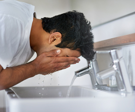 Shot of a young man washing his face at the bathroom sink