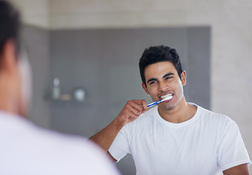 Shot of a young man brushing his teeth at home