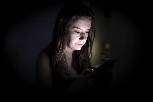 Portrait of sad young woman looking at the mobile phone screen in total darkness at her homePortrait of sad young woman looking at the mobile phone screen in total darkness at her home