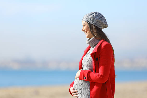 Pregnant woman taking a walk on the beach Side view portrait of a happy pregnant woman taking a walk on the beach in a sunny winter day women satisfaction decisions cheerful stock pictures, royalty-free photos & images