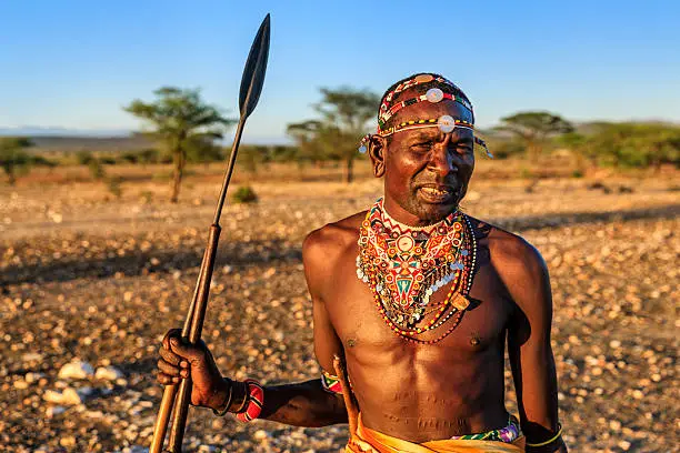 African warrior from Samburu tribe standing on savanna and holding a spear, central Kenya. Samburu tribe is one of the biggest tribes of north-central Kenya, and they are related to the Maasai.