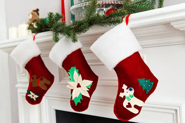 A close picture of beautifully decorated bright red Christmas socks hanging on a fireplace waiting for presents.
