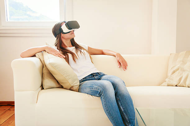 istock Young woman sitting on couch, using VR glasses 627644880