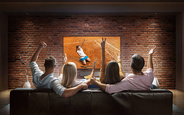 Couples watching Tennis game at home :biggrin:Two couples are cheering while watching Tennis game at home. They are sitting on a sofa in the modern living room faced to a big TV set on the front wall. tennis outfit stock pictures, royalty-free photos & images