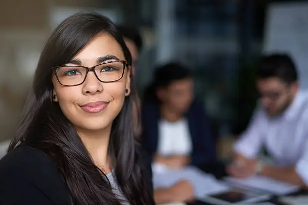 Portrait of a smiling young businesswoman in an office with colleagues in the background