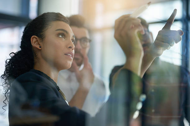 Succeeding is top priority Shot of a group of colleagues brainstorming together on a glass wall in an office writing on chalk board stock pictures, royalty-free photos & images