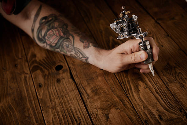 primer plano de la mano de un hombre con una pistola de tatuajes - tattoo gun fotografías e imágenes de stock
