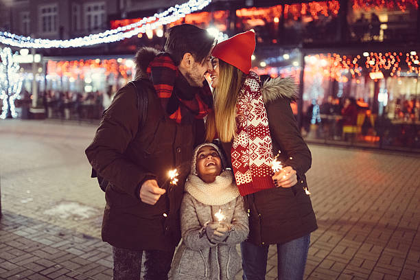Cute family wishing Happy New Year Young family with daughter celebrating New Year in the city three way kiss stock pictures, royalty-free photos & images