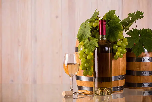 Bottle of white wine with barrels grapes and grapeleaves on glass