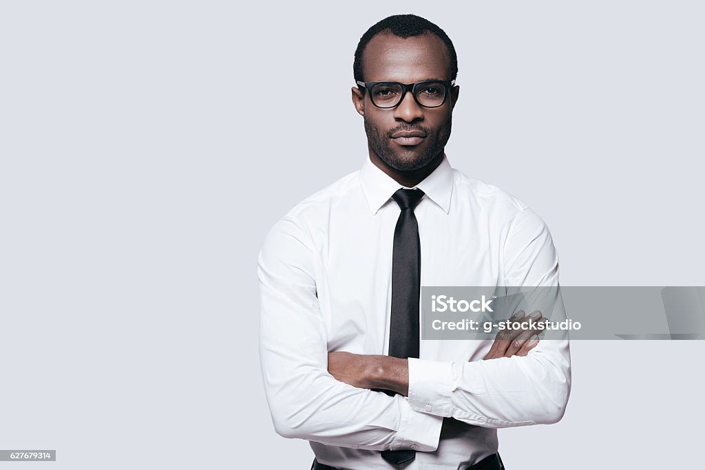 Young and successful. Handsome African man looking at camera and keeping arms crossed while standing against grey background Serious Stock Photo