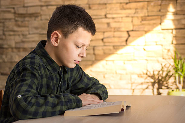 istock Young Boy Reading Book and Studying on Table at Home 627681634