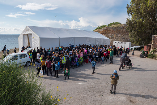 Chios, Greece - May 5, 2016: Refugees are standing in line (or getting ready to stand in line) for being served breakfast in the Souda refugee camp in Chios Town on Chios Island in Greece. The refugees have landed on Chios after crossing the Aegean Sea in flimsy inflatable boats from the shore of Turkey. The breakfast this day consisted of a sandwich and a boiled egg served by the Norwegian NGO Drop in the Ocean. The food is paid for by donations collected by the volunteers. At the moment 1,250 refugees are fed each day.