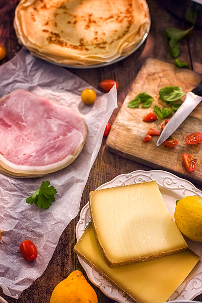 Preparing delicious crepes pancakes with ham, tomatoes and herbs baked with cheese.