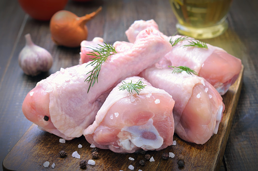 Raw chicken drumsticks and spices on wooden cutting board