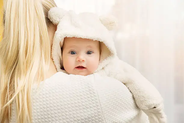 Photo of mother with her baby in fluffy bear costume over shoulder