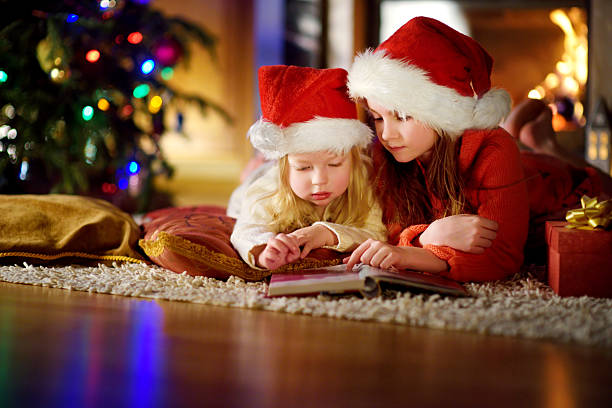 istock Two cute little sisters reading story book under Christmas tree 627744956
