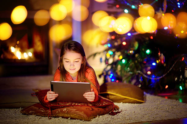 istock Adorable little girl using tablet pc by fireplace on Christmas 627745670