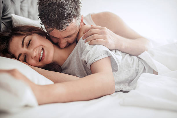 Beautiful passionate couple having sex on bed. Beautiful passionate couple having sex on bed. Man kissing on neck of woman, both lying on bed. human sexual behavior stock pictures, royalty-free photos & images