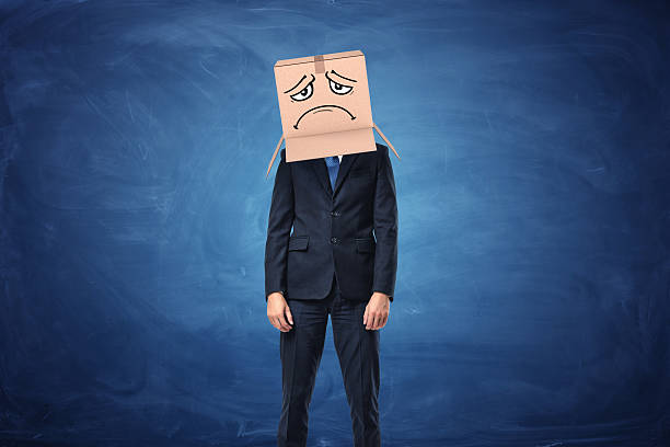 istock Businessman wearing cardboard box with drawn sad face on his 627746400