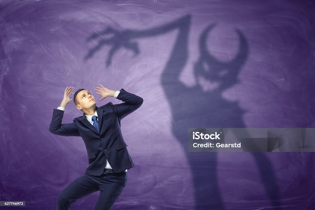Shadow of devil trying to catch the frightened businessman Shadow of devil trying to catch the frightened businessman. Temptation of money. Trapped by greedy desires. Personal demons. Business issues. Monster - Fictional Character Stock Photo
