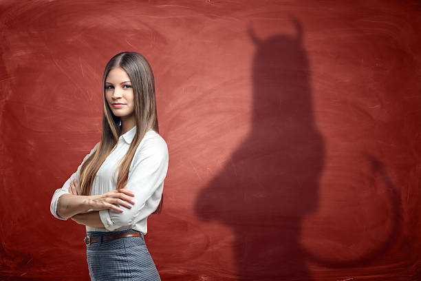 joven empresaria proyecta sombra de diablo sobre naranja oxidada - demonio mujer fotografías e imágenes de stock