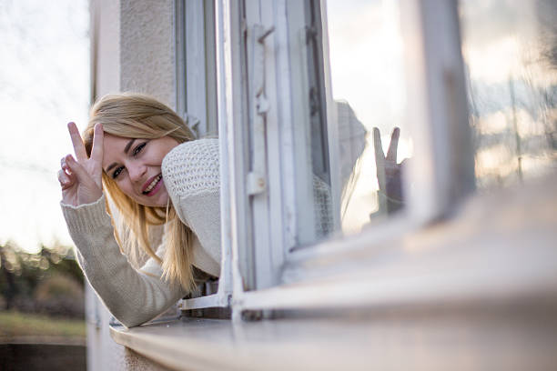 istock Girl showing peace sign from house window 627759230