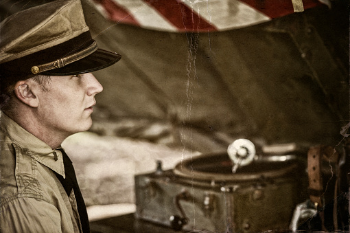 Aged Photo of Naval officer enjoying some down time in his tent listening to his photograph play records.  Grain and cracking from aging process... NOTE: These are authentic, professional WWII reenactment actors and models wearing authentic WWII era US Army military uniforms and 